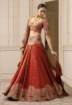 a woman in a red and gold lehenga is posing for the camera with her hand on her hip