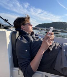 a man laying on the back of a boat while holding a cell phone in his hand