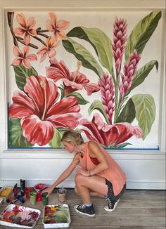 a woman kneeling down in front of a painting on the wall with flowers painted on it