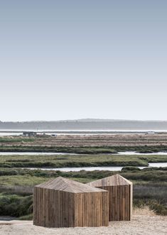 two wooden structures sitting on top of a sandy beach next to the ocean and grass