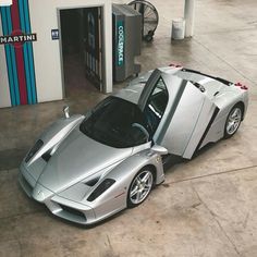 a silver sports car parked in front of a gas station with its door open and the hood up