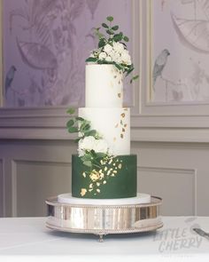 a white and green wedding cake sitting on top of a silver platter with flowers