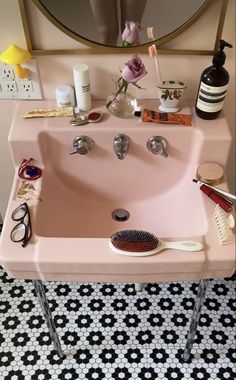 a pink sink with hair brushes and other items on it in front of a mirror