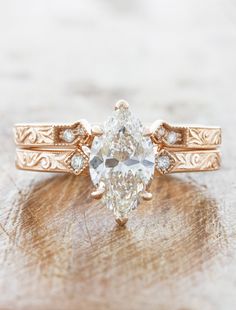 a close up of a ring with a pear shaped diamond in the center on top of a piece of wood