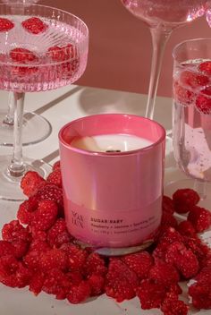 raspberry scented candle surrounded by wine glasses and strawberries on a white table