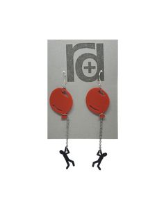 two red and black earrings hanging from hooks on a white background with the letter g