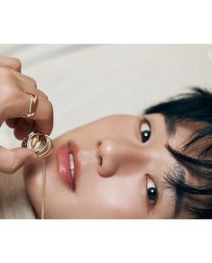 a woman holding onto a gold ring while laying on top of a white bed next to her face