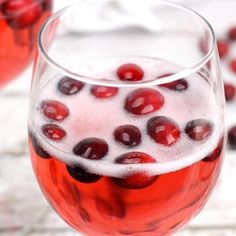 two glasses filled with red wine and cranberries on top of a white table