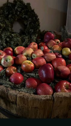 a large basket filled with lots of red and green apples next to a wreath on top of a wooden table