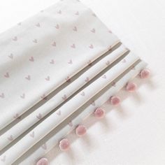 three pieces of white fabric with pink hearts on them and two pairs of knitting needles