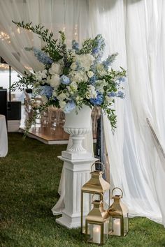 a white vase filled with blue and white flowers on top of a lush green field