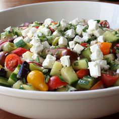 a white bowl filled with cucumber, tomato and feta cheese salad on top of a wooden table