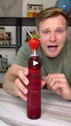 a man is holding up a bottle with a strawberry on it and pointing to the top