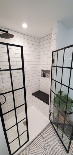 a white tiled bathroom with black trim and glass partitions on the shower wall, along with a patterned rug