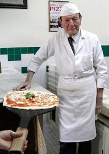 an old man in a white chef's coat holding a pizza