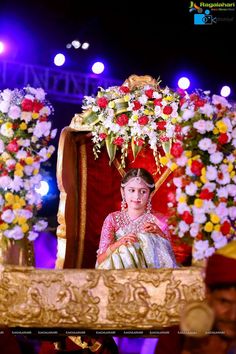 a woman in a white and red dress sitting on a stage with flowers around her head