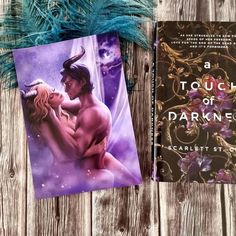 two books are laying next to each other on a wooden surface, one is titled a touch of darkness