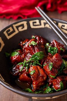 a bowl filled with meat and greens on top of a wooden table next to chopsticks