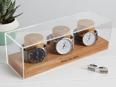 three watches in a clear display case on a white table next to a potted plant