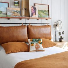 a bed with brown pillows and pictures on the wall above it, along with an orange throw pillow