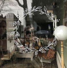 the reflection of a person sitting in a chair behind a glass window with a wreath drawn on it