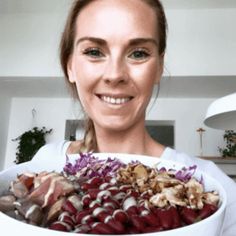 a woman holding a large bowl full of food in front of her face and smiling at the camera