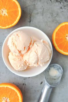 an orange ice cream in a white bowl next to sliced oranges