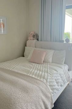 a white bed sitting in a bedroom next to a window with curtains on the windowsill