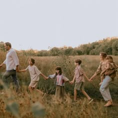 a group of people holding hands and walking through a grass field with trees in the background