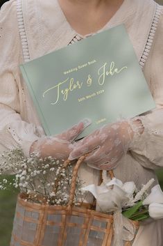 a close up of a person holding a basket with flowers and a book in it