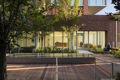 a person sitting on a bench in front of a building with lots of windows and trees