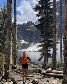 a woman in an orange vest is standing on rocks near some trees and looking at the camera