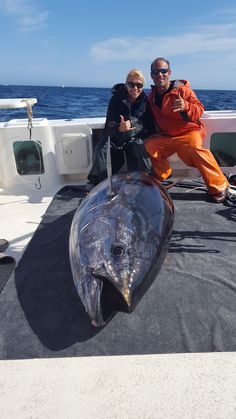 two people on a boat posing for a photo with a big fish in the water