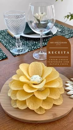 a wooden table topped with a yellow flower next to wine glasses and napkins on top of it