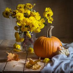 a vase filled with yellow flowers sitting on top of a wooden table next to a pumpkin