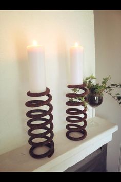 two white candles sitting on top of a table next to some brown spiral candle holders