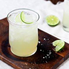 a drink on a wooden tray with limes around it