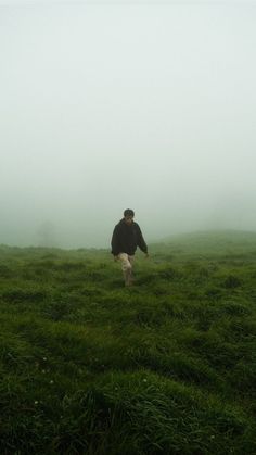 a man walking across a lush green field on a foggy day in the countryside