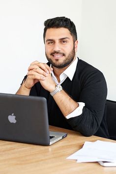 a man sitting at a table in front of a laptop computer with his hands clasped