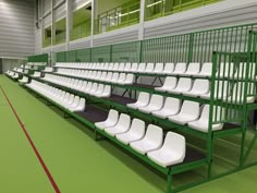 rows of white plastic chairs in an empty sports stadium or gym area with green flooring