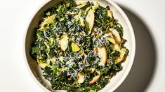 a bowl filled with spinach and apples on top of a white countertop next to a spoon