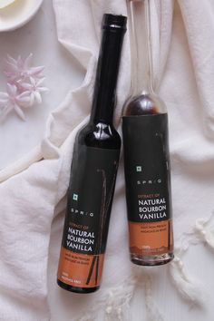 two bottles of vanilla syrup sitting next to each other on a white cloth with flowers