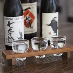 three wine glasses on a wooden tray with bottles in the background and two empty glass cups sitting next to each other