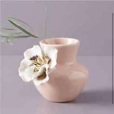 a white flower in a pink vase on a gray surface with an olive branch sticking out of it