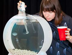 a woman holding a red cup in front of a fish tank filled with white balls