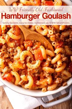 a white bowl filled with hamburger goulash and pasta on top of a wooden table