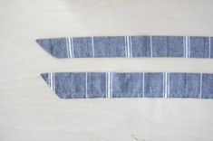 two ties laid out on top of each other in front of a wooden surface with white and blue stripes