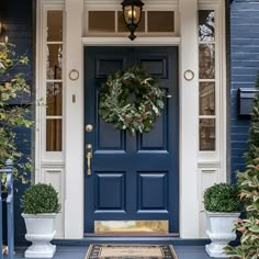 a blue front door with two potted plants and a wreath on the entrance step