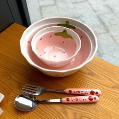 three spoons and two forks are sitting on a table next to a bowl with apples painted on it