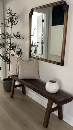 a wooden bench sitting under a mirror next to a potted plant and a white vase